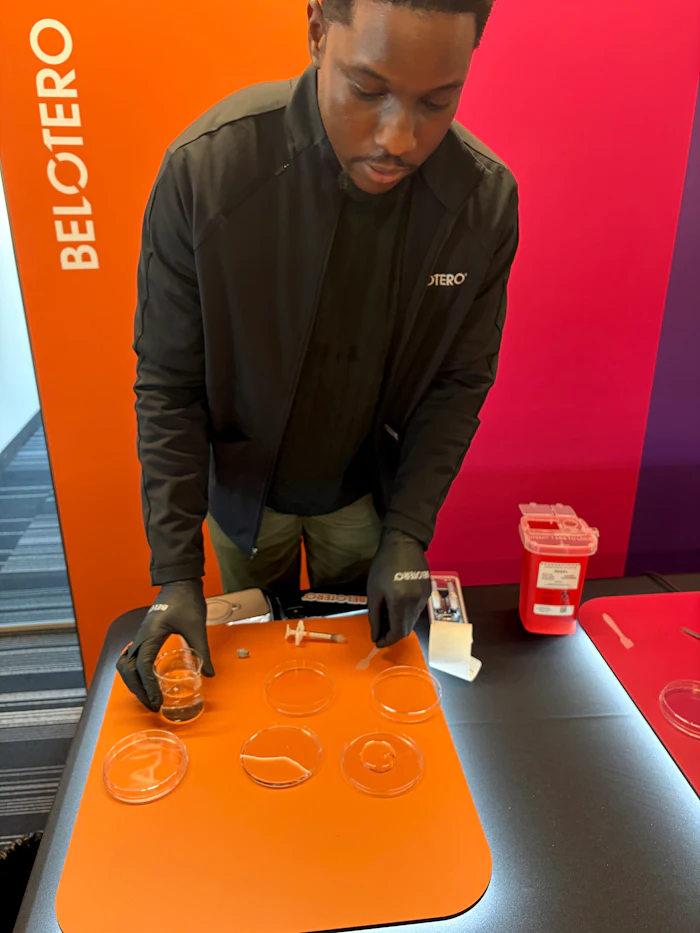 Man in black jacket demonstrating laboratory procedure with petri dishes at Belotero branded event table