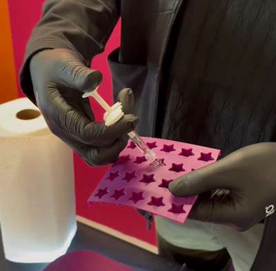 Gloved hands pipetting liquid into pink star-shaped silicone mold during laboratory procedure