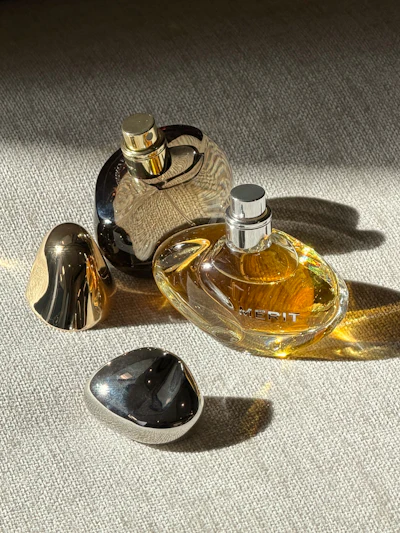 Three luxury perfume bottles with gold and black caps arranged on a neutral textured surface with dramatic shadows
