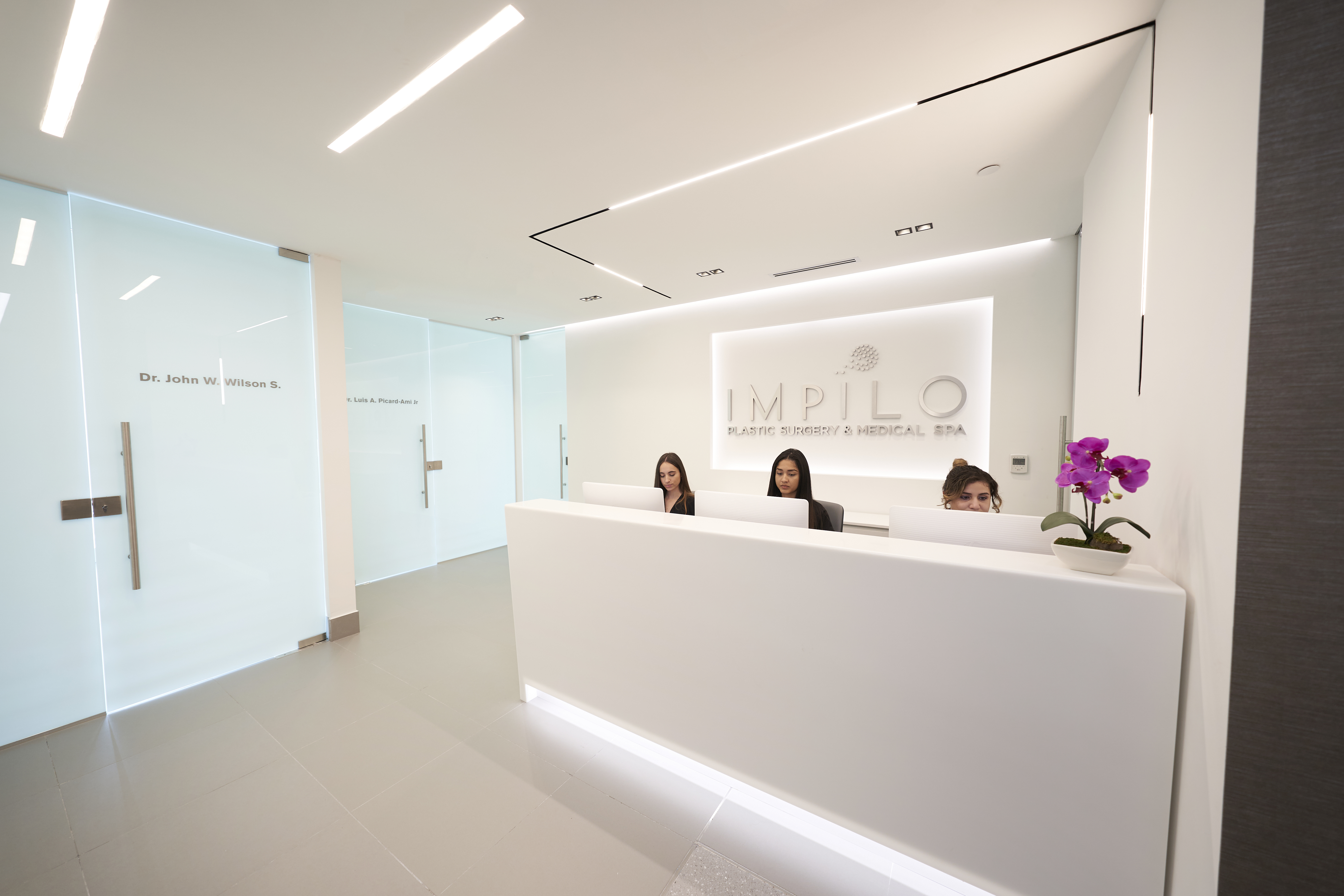 Modern medical spa reception area with white desk, three staff members, and IMPILO branding on wall