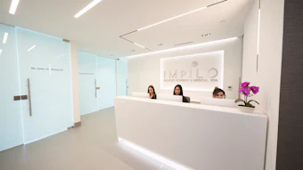 Modern medical spa reception area with white desk, three staff members, and IMPILO branding on wall