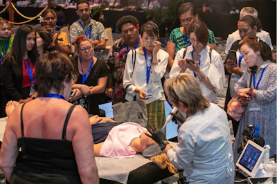 Healthcare professionals in blue lanyards observe a clinical demonstration or training session at a medical conference.