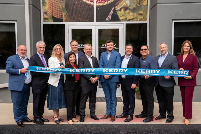 Group of business professionals holding blue Kerry ribbon at ribbon-cutting ceremony outside building