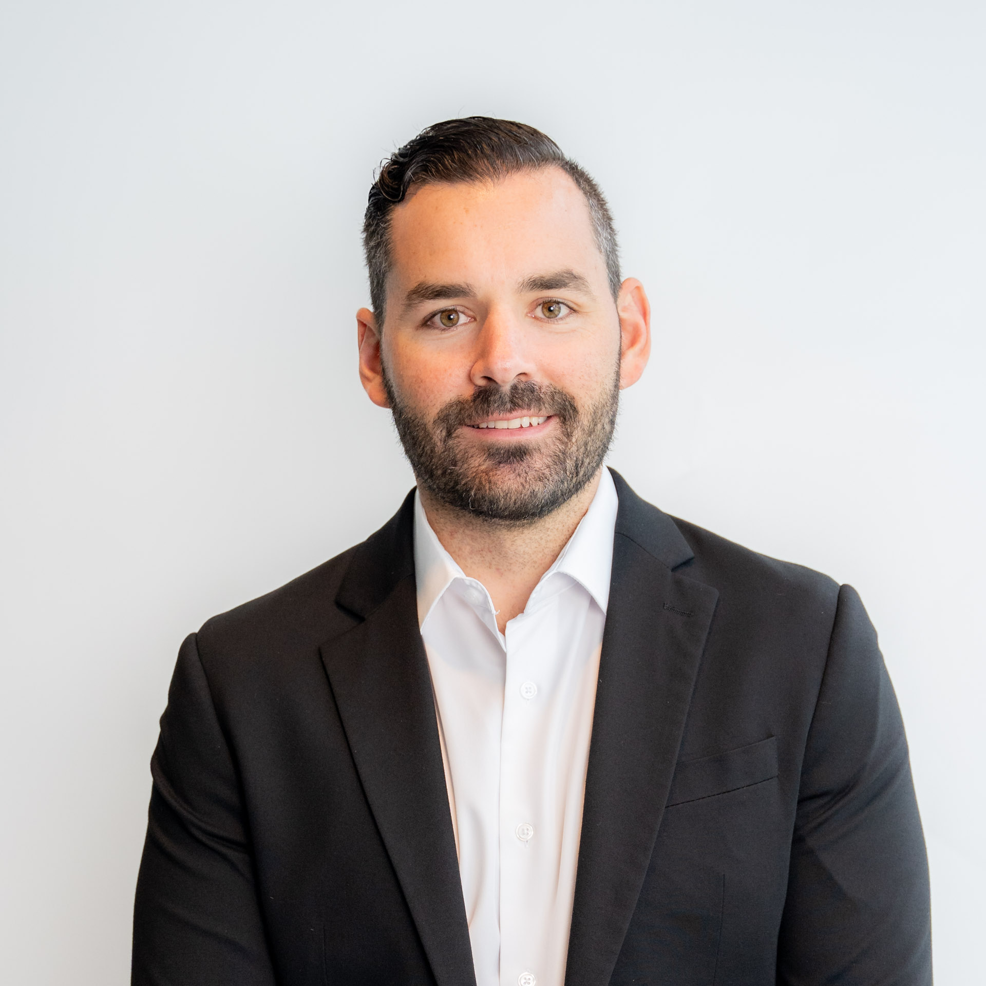Professional headshot of a bearded man in black blazer and white shirt against neutral background