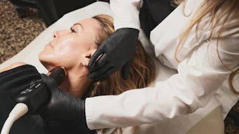 Aesthetician performing facial treatment on client using professional handheld device