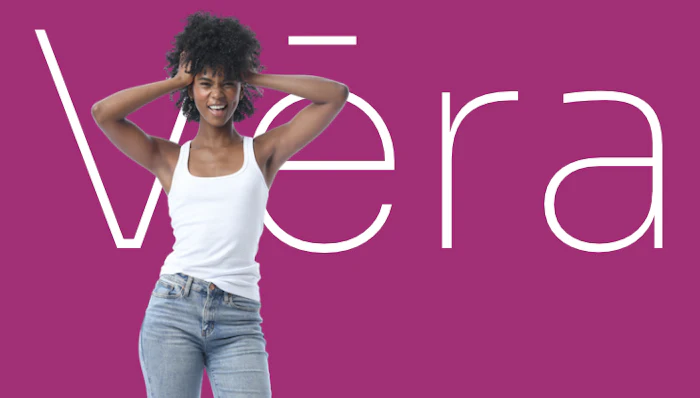 Woman in white tank top and jeans posing against magenta background with 'Vera' text overlay
